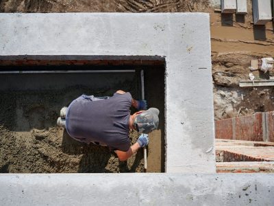 Top view of bricklayer in protective gloves working with sand and doing walls on fresh air. Concept of process building walls and modern house with good weather and modern equipments.